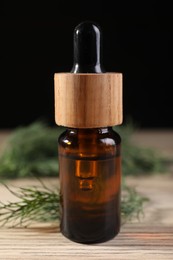 Bottle of essential oil and fresh dill on wooden table, closeup