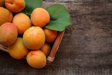 Photo of Basket with delicious ripe apricots on wooden table, top view. Space for text