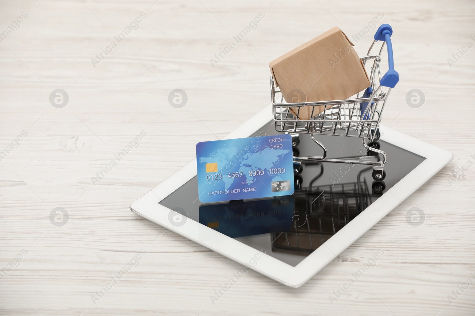Photo of Online payment concept. Small shopping cart with bank card, box and tablet on white table, space for text