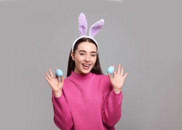 Photo of Happy woman in bunny ears headband holding painted Easter eggs on grey background