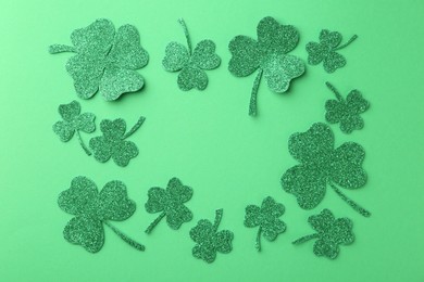 Photo of St. Patrick's day. Frame of shiny decorative clover leaves on green background, flat lay. Space for text