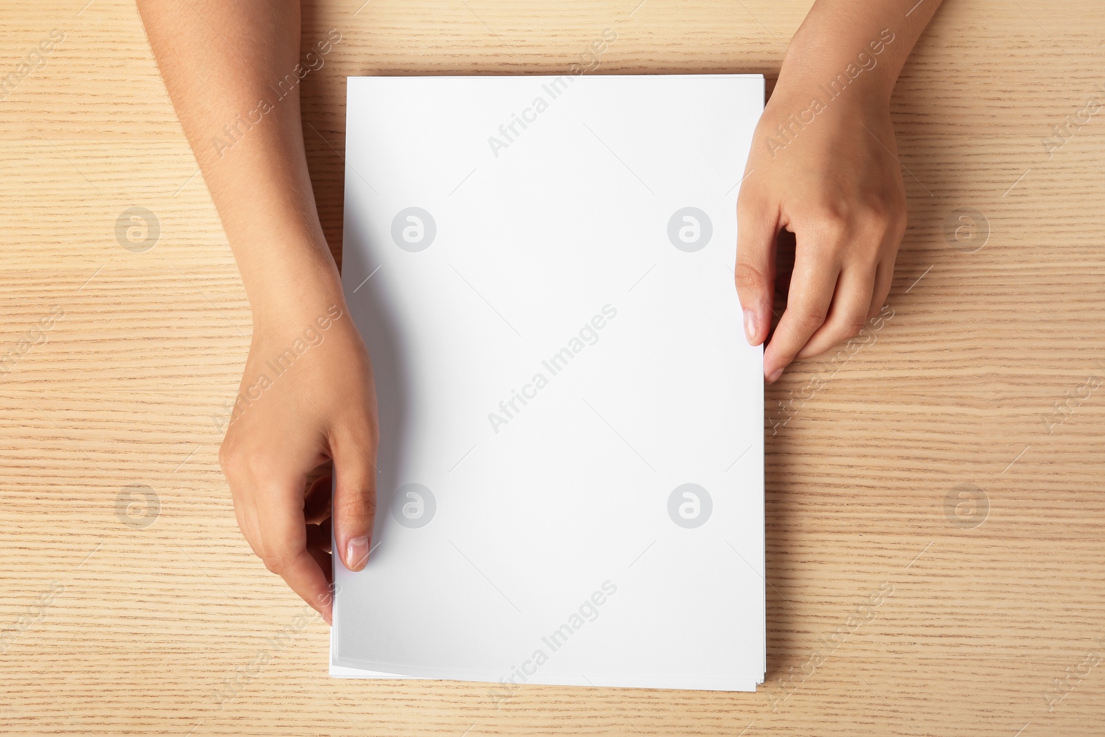 Photo of Woman holding blank paper sheets for brochure at wooden table, top view. Mock up