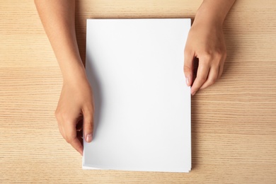 Photo of Woman holding blank paper sheets for brochure at wooden table, top view. Mock up