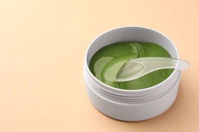 Photo of Jar of under eye patches and spoon on beige background, closeup with space for text. Cosmetic product
