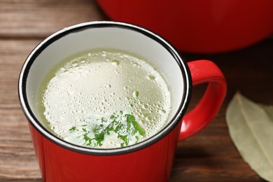 Red mug with tasty bouillon on wooden table, closeup