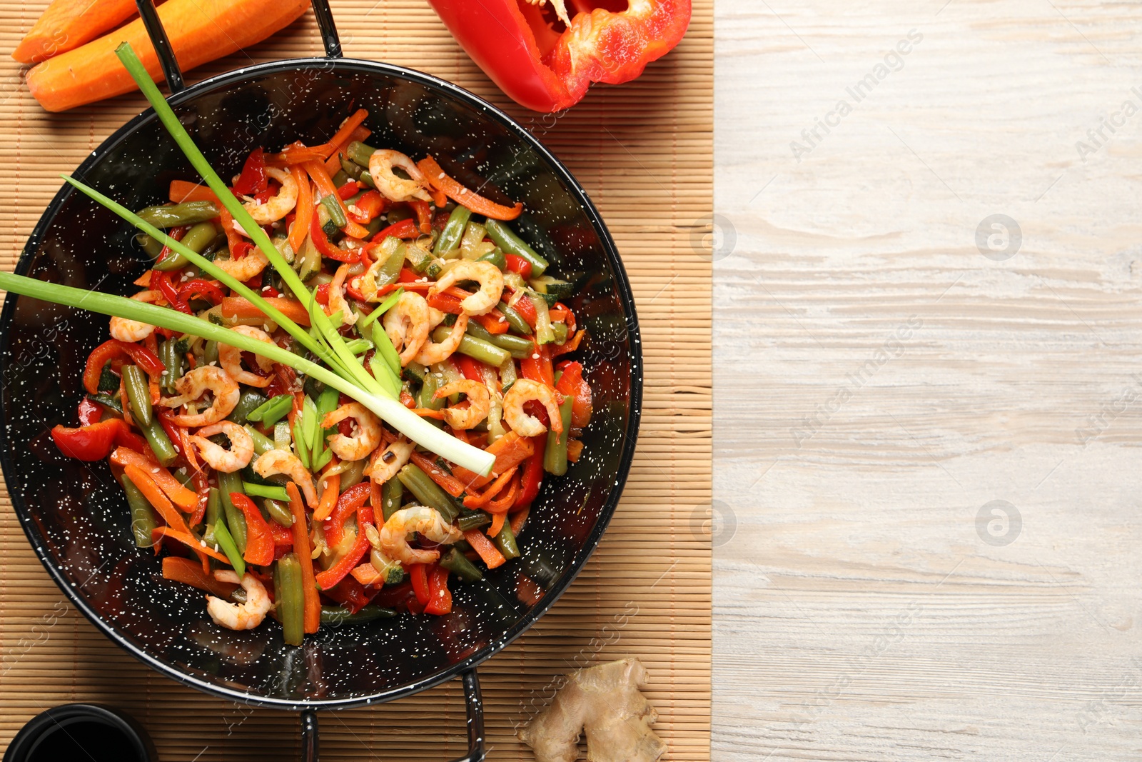 Photo of Shrimp stir fry with vegetables in wok and ingredients on wooden table, flat lay. Space for text