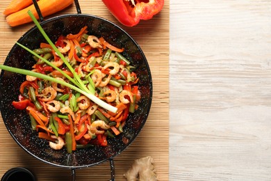 Photo of Shrimp stir fry with vegetables in wok and ingredients on wooden table, flat lay. Space for text