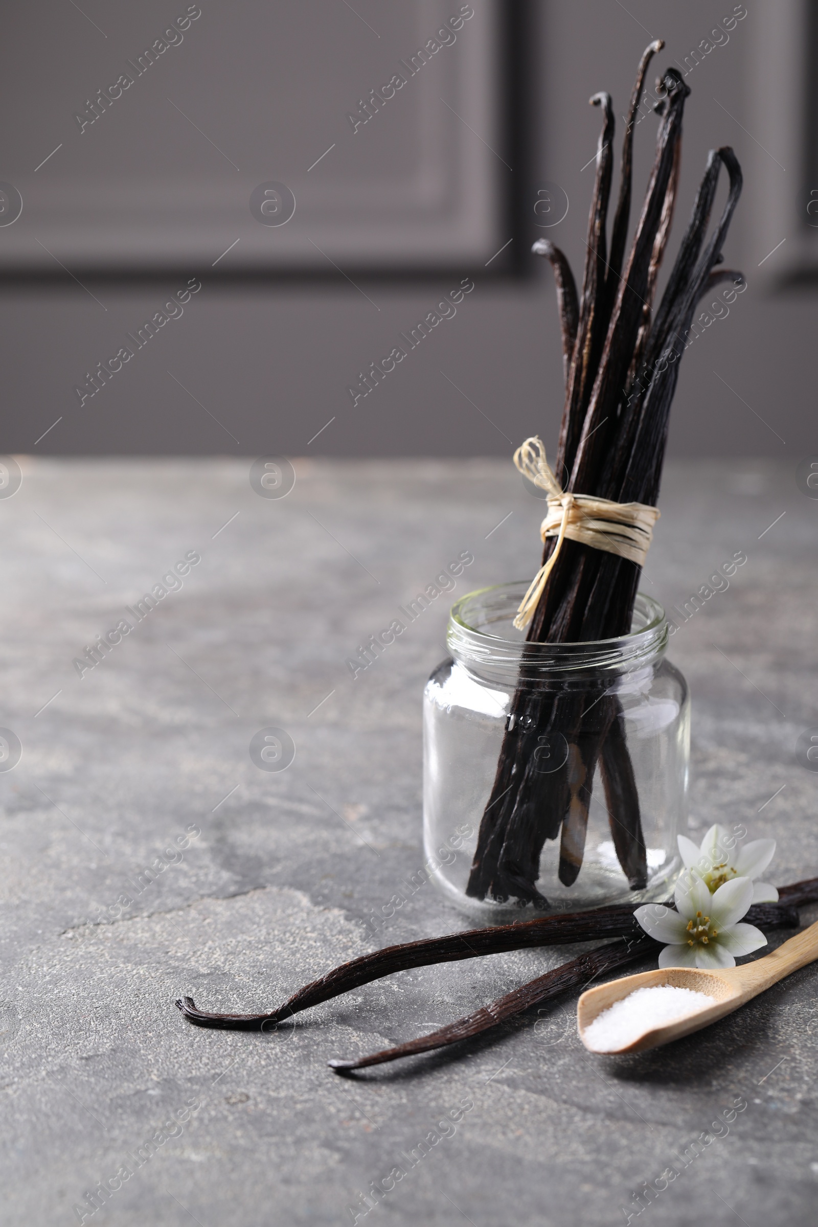 Photo of Spoon with sugar, flowers and vanilla pods on grey textured table. Space for text