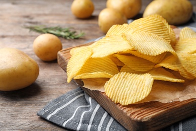 Board with crispy potato chips on wooden table. Space for text