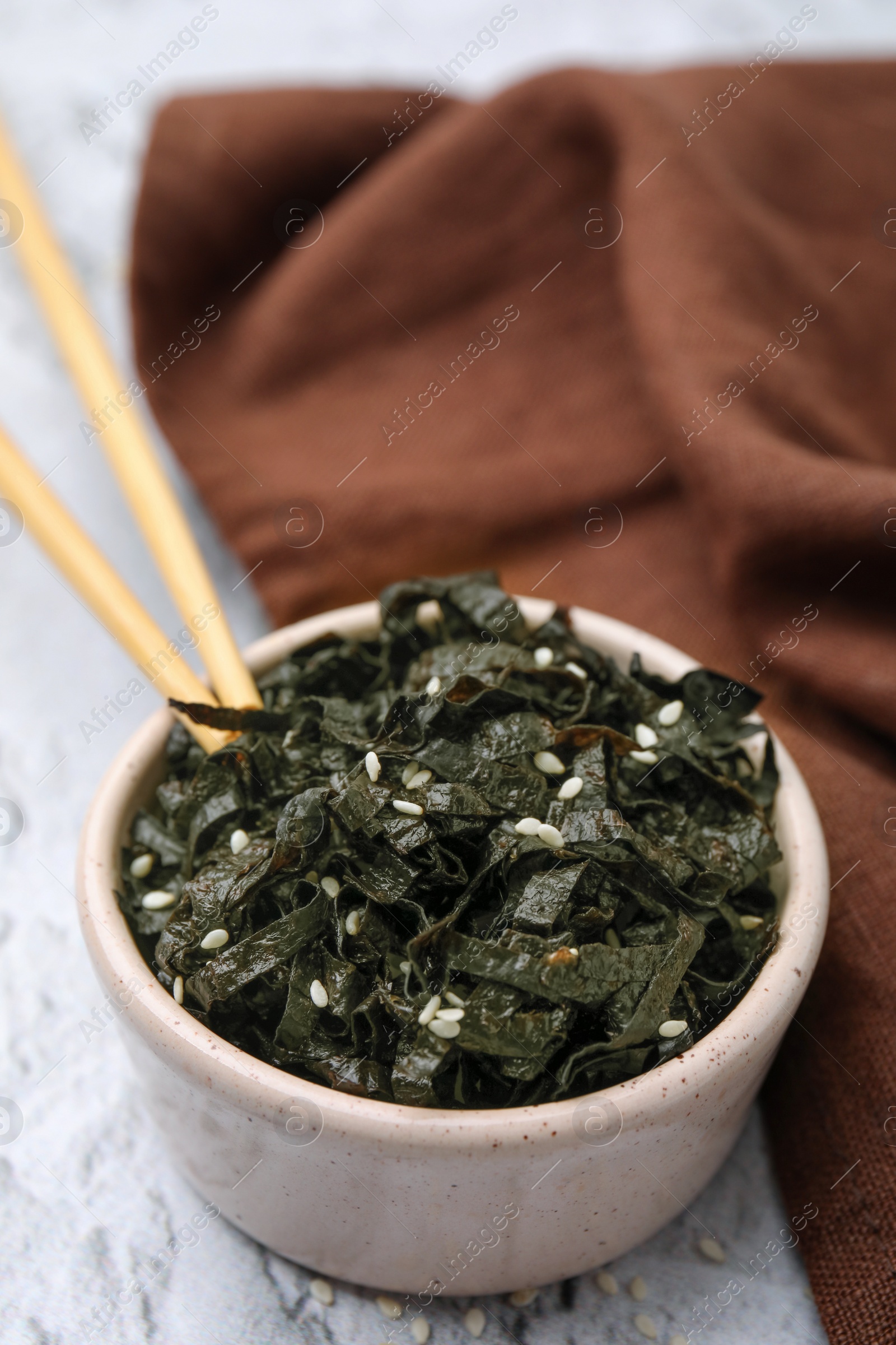 Photo of Chopped nori sheets with sesame and chopsticks on white textured table, closeup