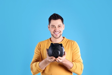 Man with piggy bank on color background