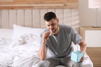 Photo of Ill man with nasal spray and box of tissues on bed at home