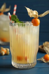 Photo of Refreshing cocktail decorated with physalis fruit on blue wooden table
