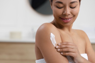 Photo of Young woman applying body cream onto arm in bathroom, closeup. Space for text