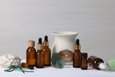 Photo of Different aromatherapy products, burning candle and eucalyptus leaves on white wooden table against light background