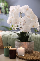Photo of Beautiful white orchids and candles on table in bedroom. Interior design
