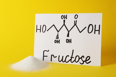 Pile of sugar and word Fructose with drawn scheme on paper against yellow background