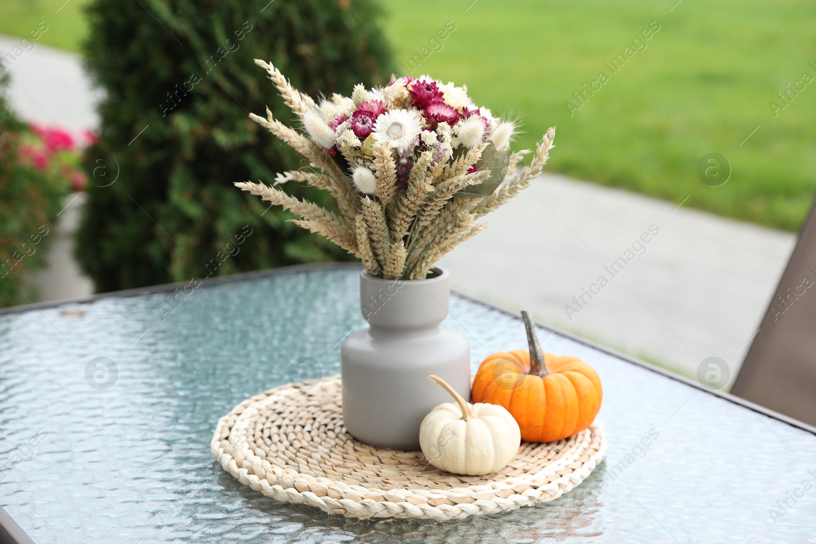 Photo of Beautiful bouquet of dry flowers and small pumpkins on glass table outdoors