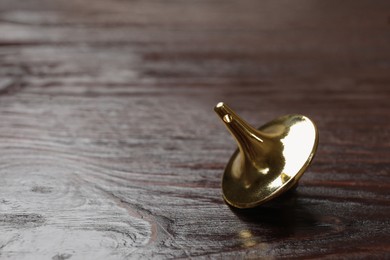 Photo of One metal spinning top on wooden table, closeup. Space for text