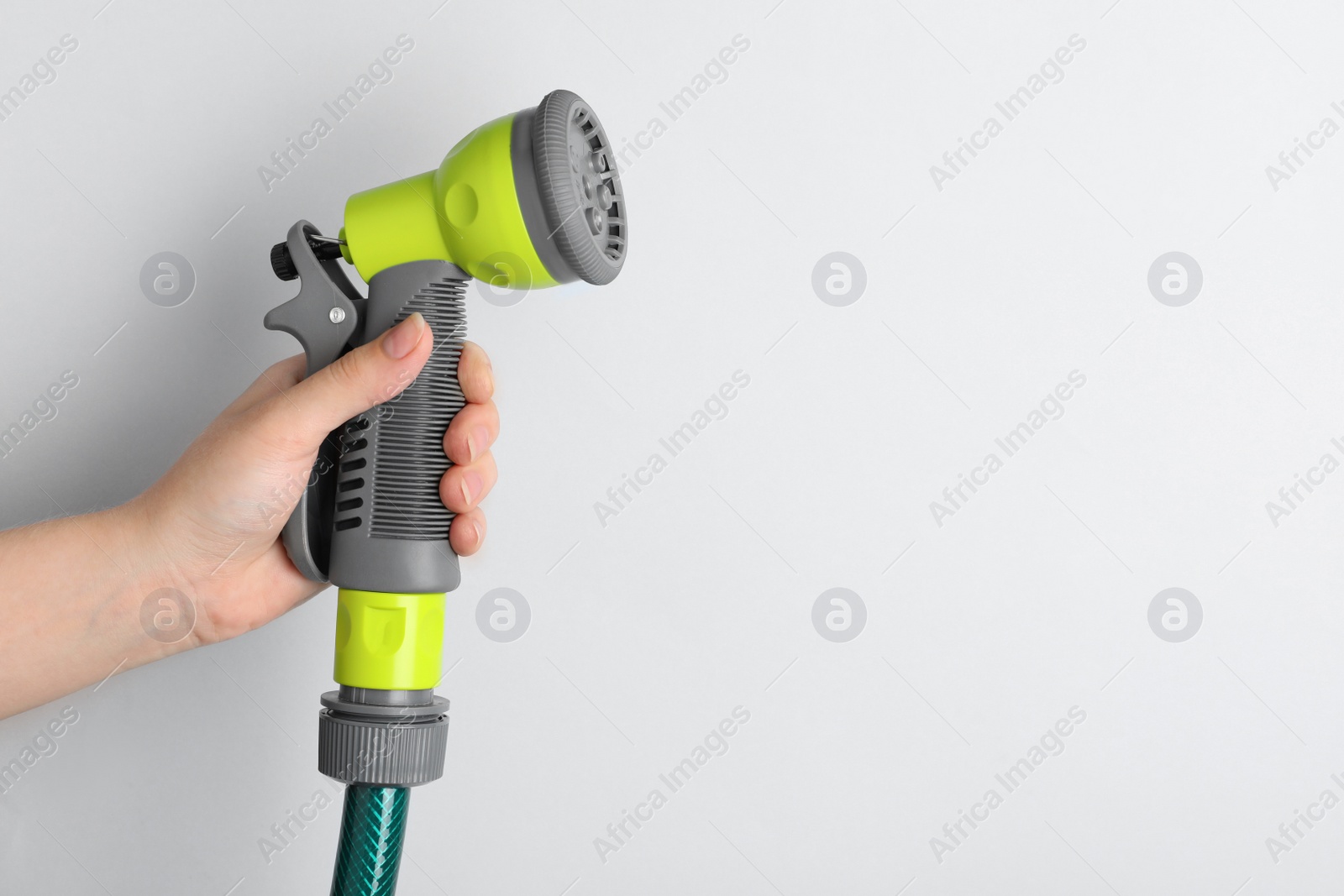 Photo of Woman holding watering hose with sprinkler on light background, closeup. Space for text