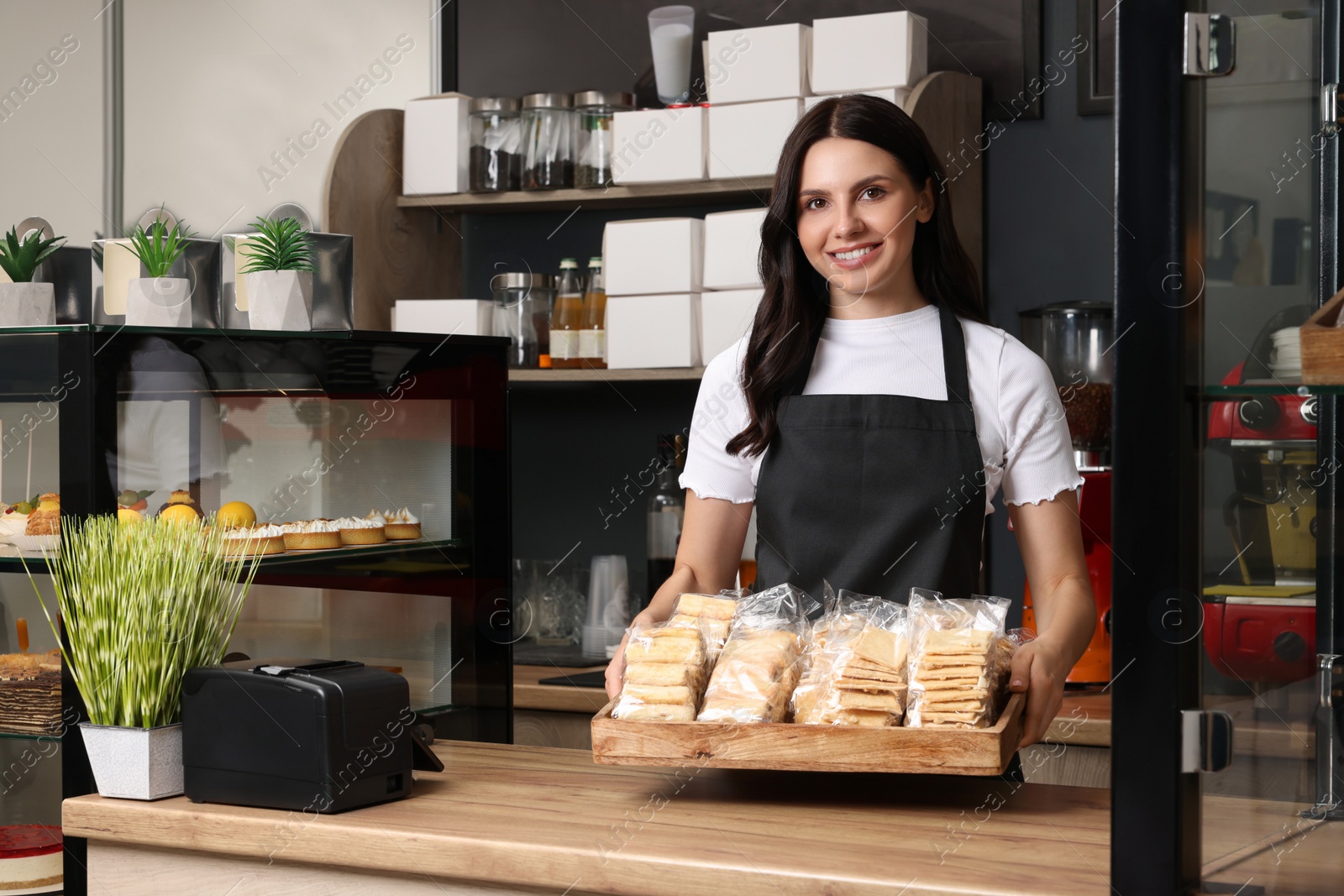 Photo of Business owner in her cafe. Happy woman holding tray with delicious pastries at desk