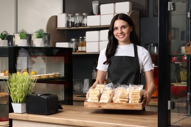 Photo of Business owner in her cafe. Happy woman holding tray with delicious pastries at desk