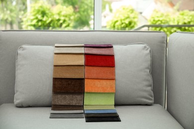 Photo of Catalog of colorful fabric samples on grey sofa indoors