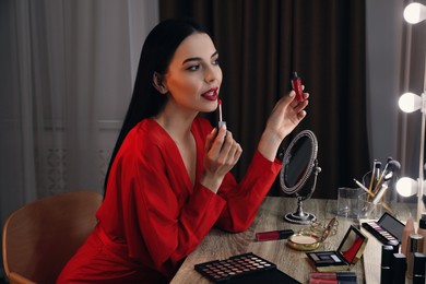 Beautiful woman applying makeup near mirror in room