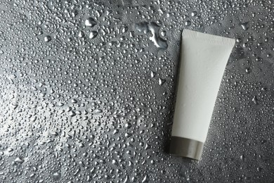 Moisturizing cream in tube on silver background with water drops, top view. Space for text