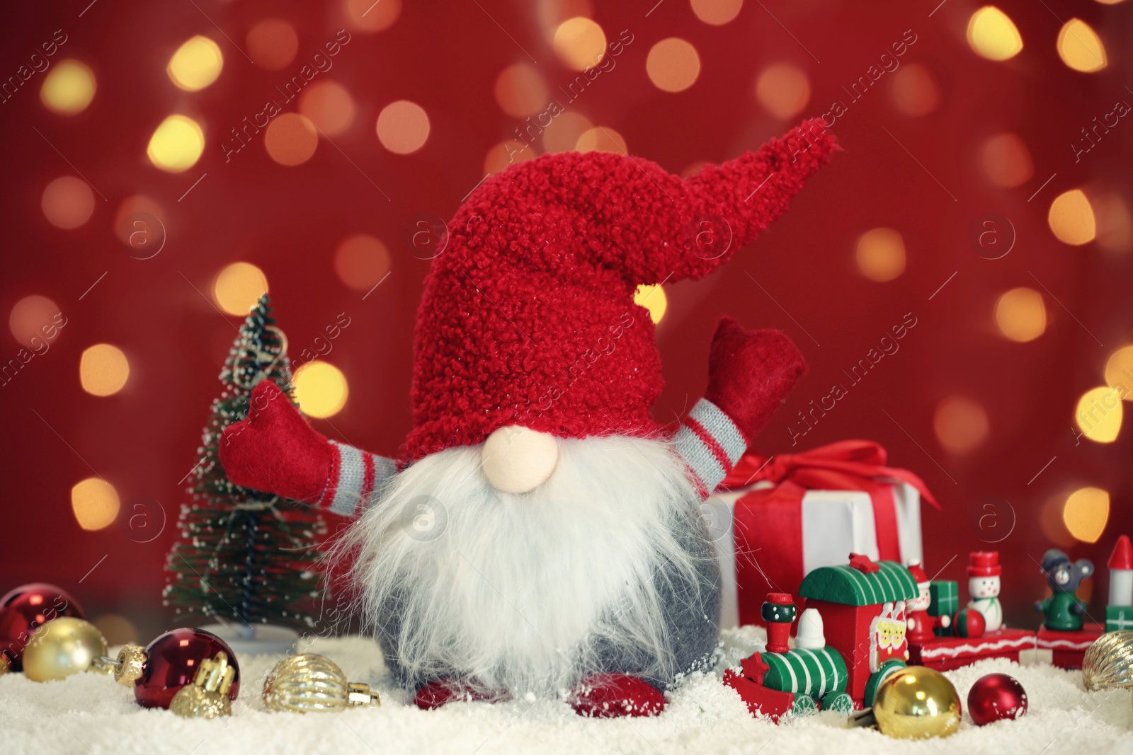 Photo of Cute Christmas gnome, gift box and festive decor on snow against blurred lights