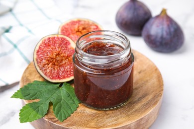 Glass jar of tasty sweet fig jam and fruits on white marble table