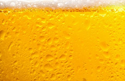 Photo of Glass of tasty cold beer with foam and condensation drops on white background, closeup