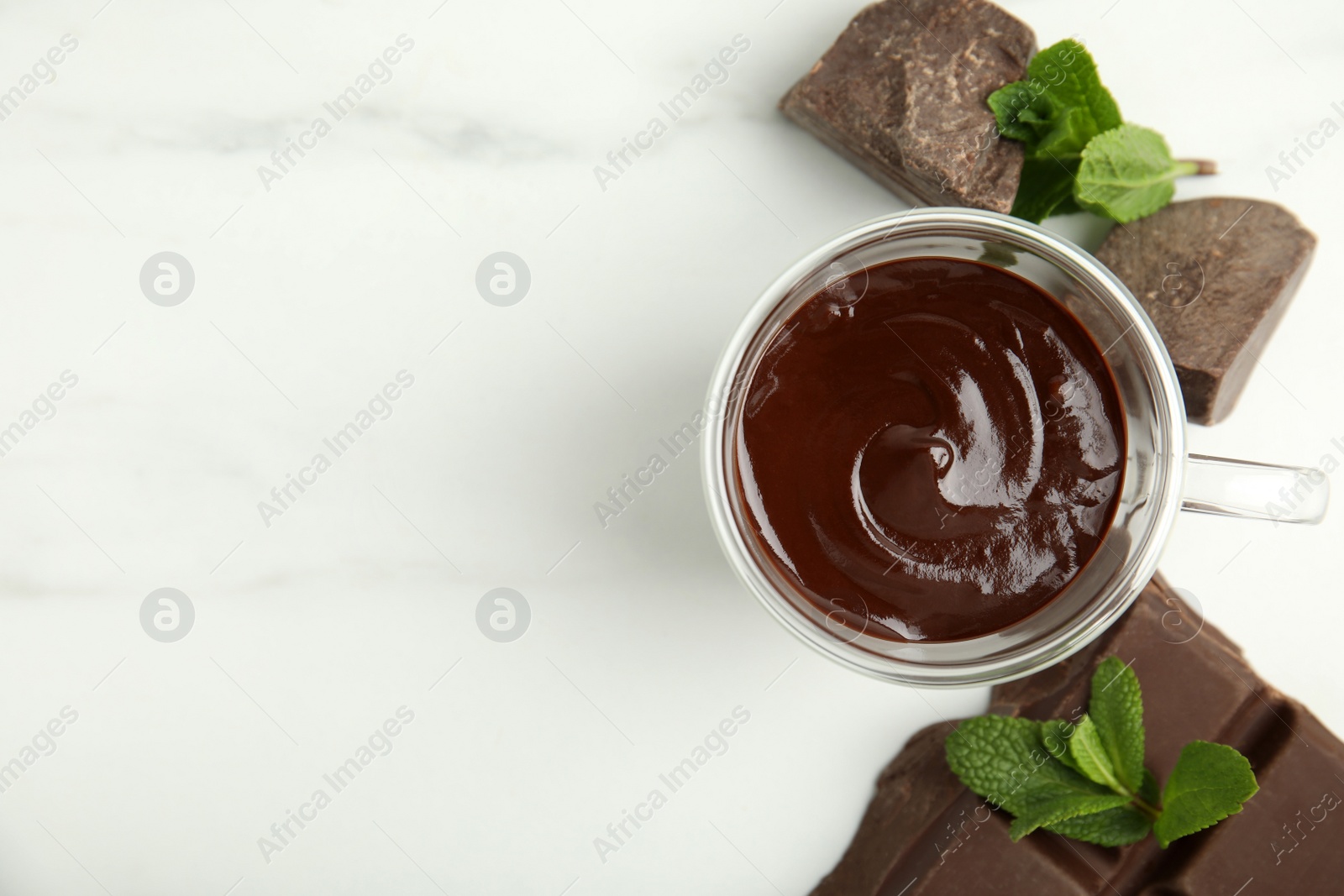 Photo of Glass cup of delicious hot chocolate, chunks and fresh mint on white marble table, flat lay. Space for text