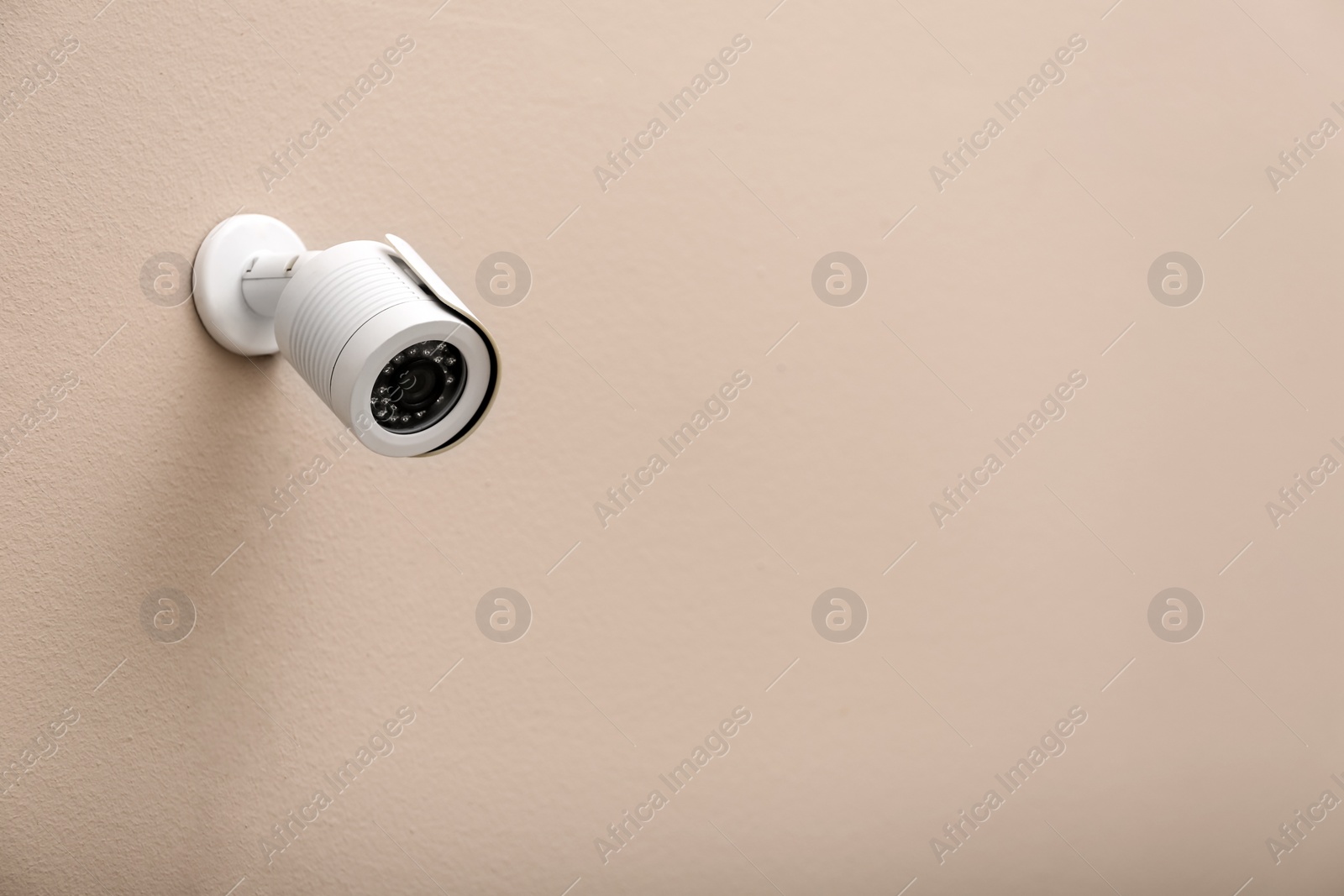 Photo of Modern CCTV security camera on beige wall. Space for text