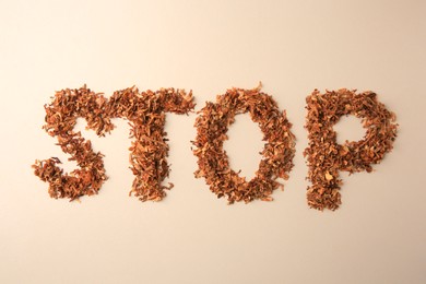 Photo of Word Stop made of dry tobacco on beige background, flat lay. Quitting smoking concept