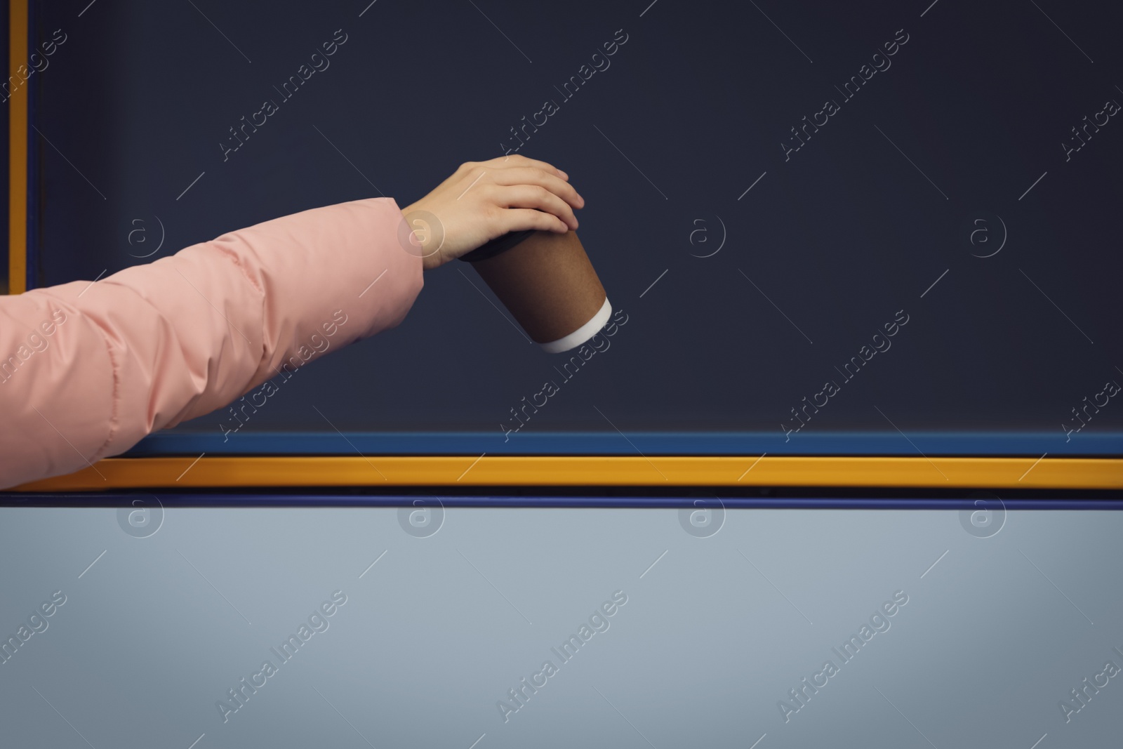 Photo of Woman throwing paper coffee cup into garbage bin outdoors, closeup. Waste sorting