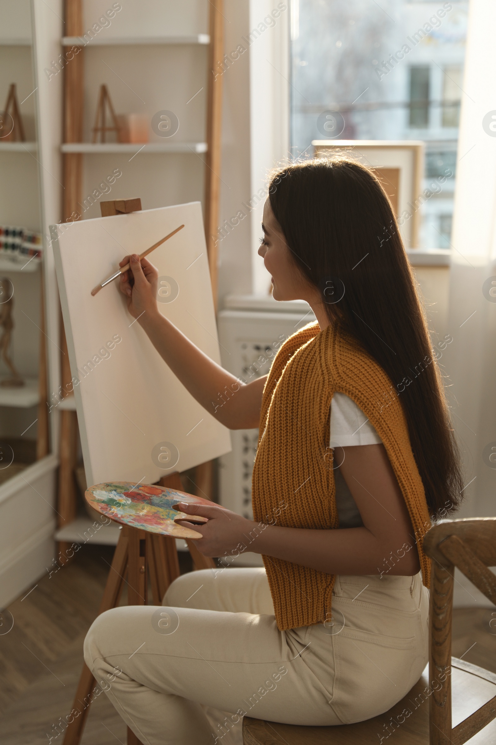 Photo of Beautiful young woman drawing on easel at home