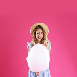 Photo of Happy young woman with cotton candy on pink background