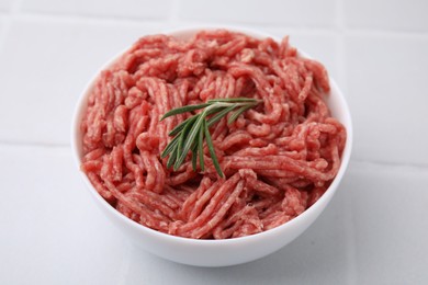 Fresh raw ground meat and rosemary in bowl on white tiled table, closeup