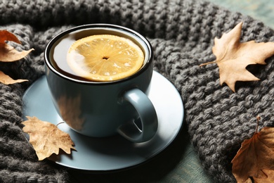 Cup of hot cozy drink, autumn leaves and knitted scarf on table