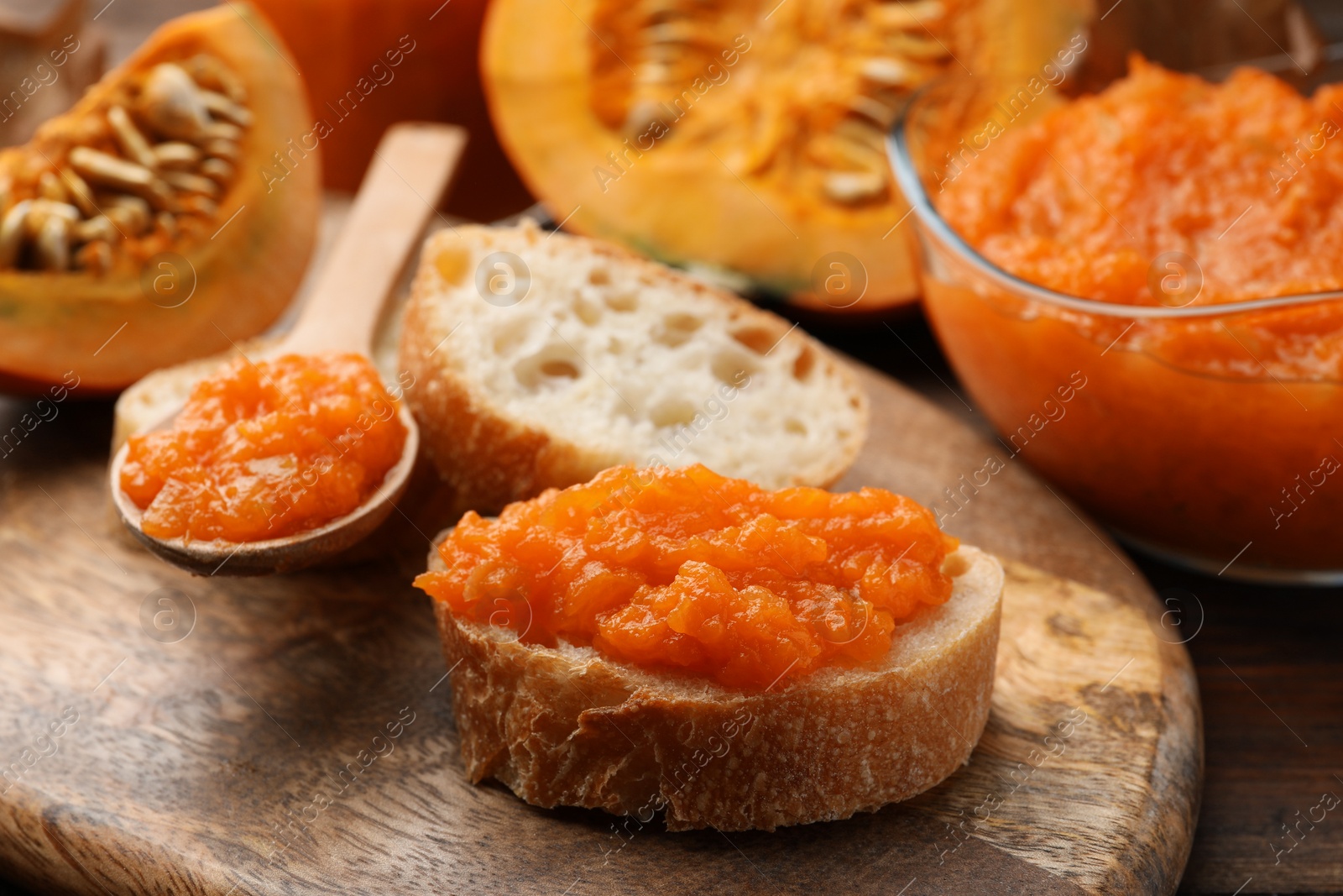 Photo of Slices of bread with delicious pumpkin jam and fresh pumpkin on wooden table, closeup