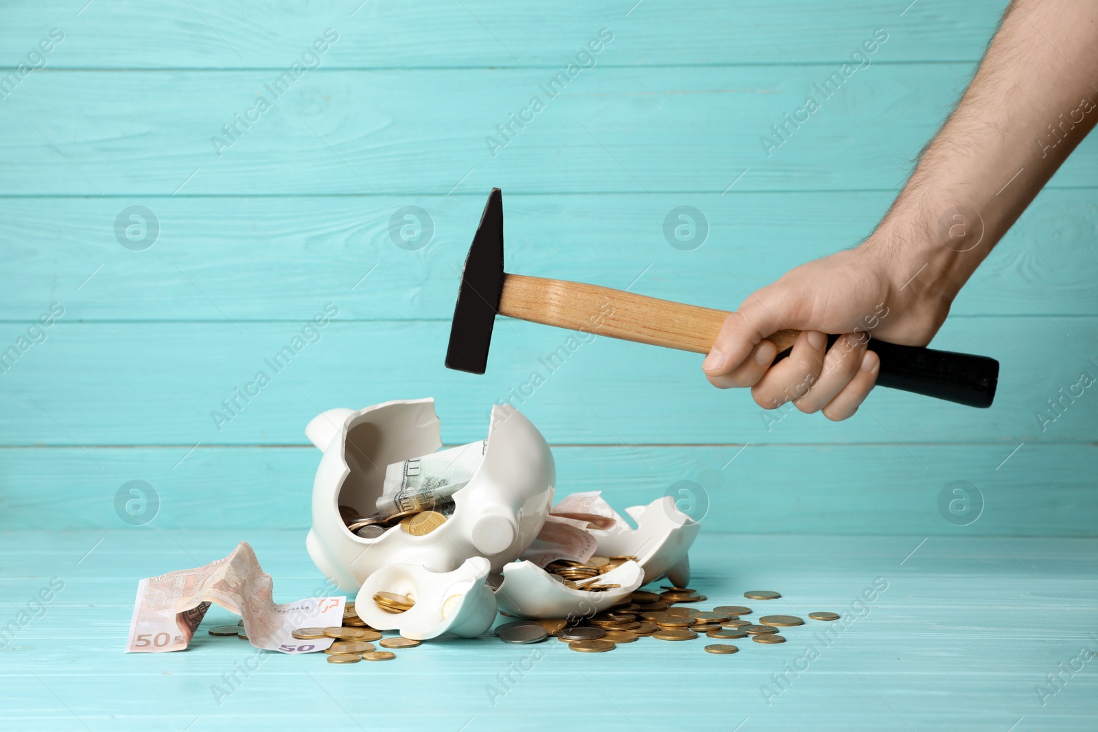 Photo of Man breaking piggy bank with hammer on table