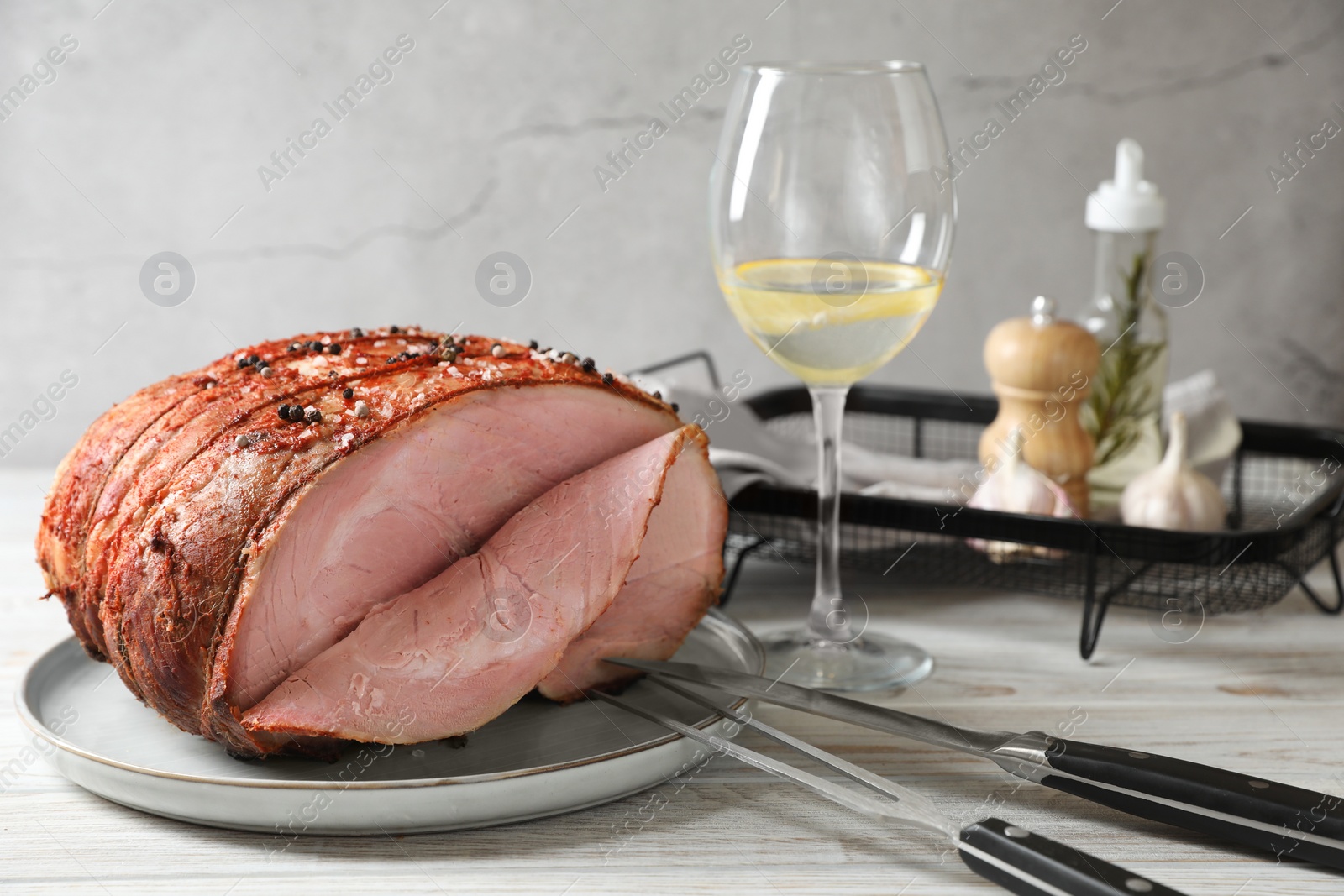 Photo of Delicious baked ham, carving fork, knife and glass of drink on white wooden table