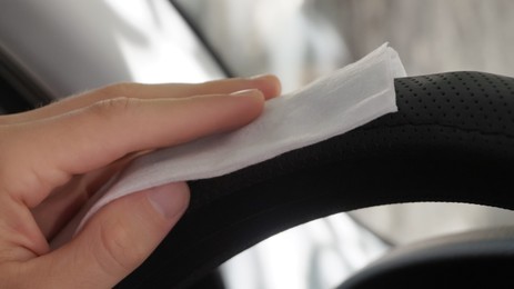 Photo of Man cleaning steering wheel with wet wipe in car, closeup. Protective measures
