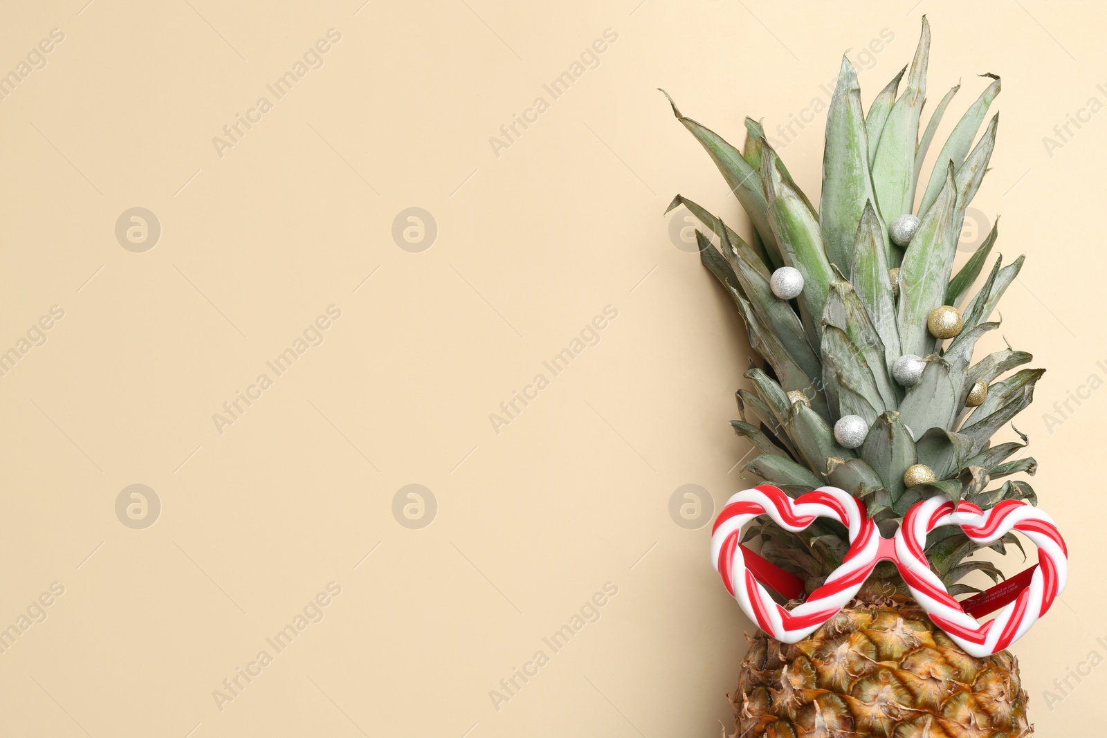 Photo of Top view of pineapple with funny glasses and festive decor on beige background, space for text. Creative concept