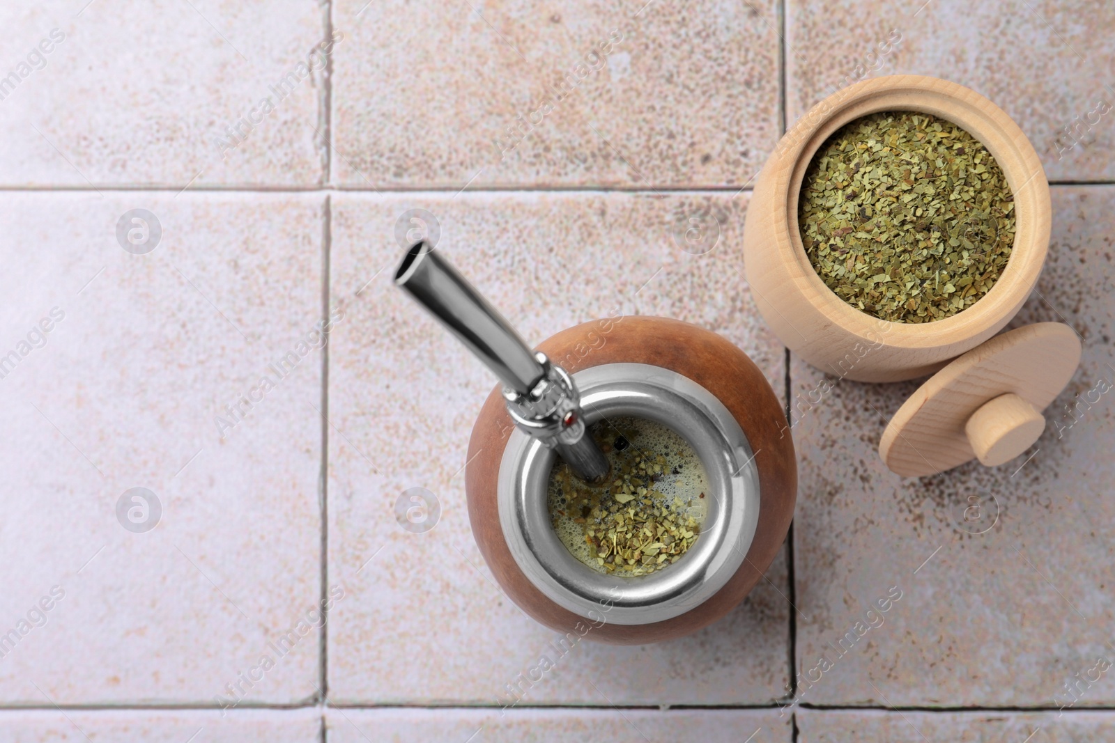 Photo of Calabash with bombilla and jar of mate tea leaves on tiled table, flat lay. Space for text