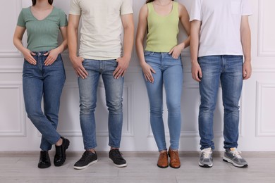 Photo of Group of people in stylish jeans near white wall indoors, closeup