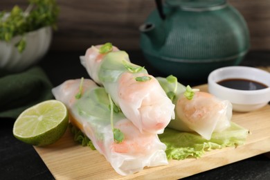 Photo of Delicious spring rolls, lettuce, lime and soy sauce on black table, closeup