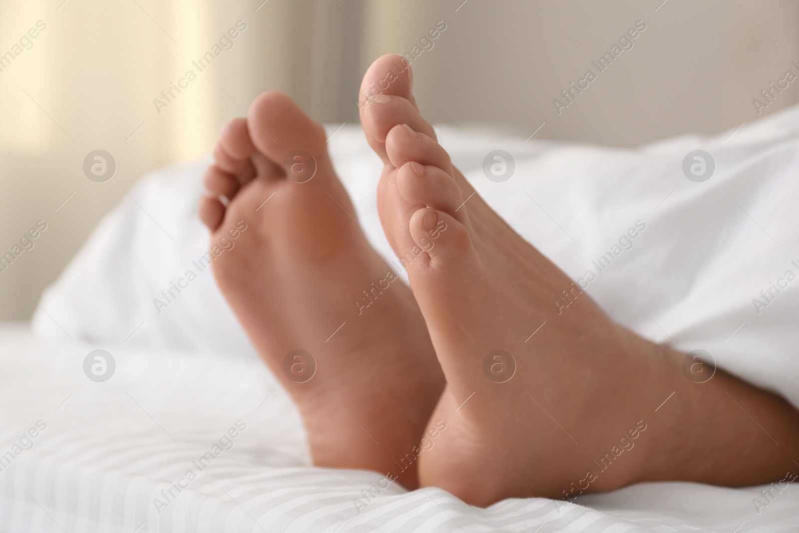 Photo of Person in bed with white linens at home, closeup on feet