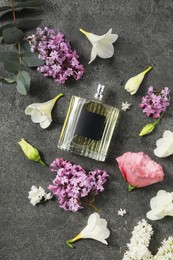 Bottle of luxury perfume and floral decor on dark grey table, flat lay